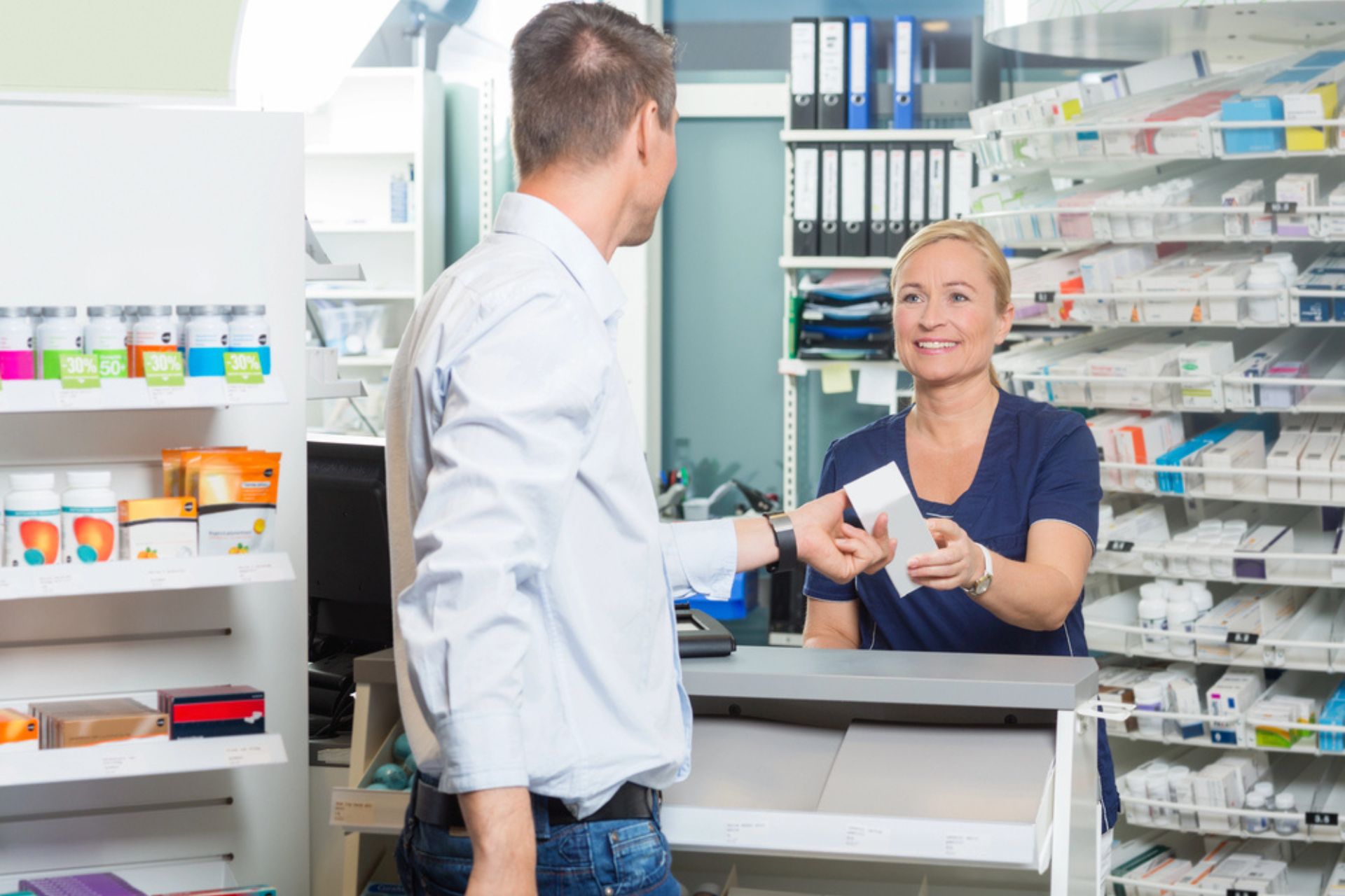 Pharmacienne souriante aidant un client à récupérer ses médicaments, illustrant l'importance d'un plan de continuité des activités en pharmacie.