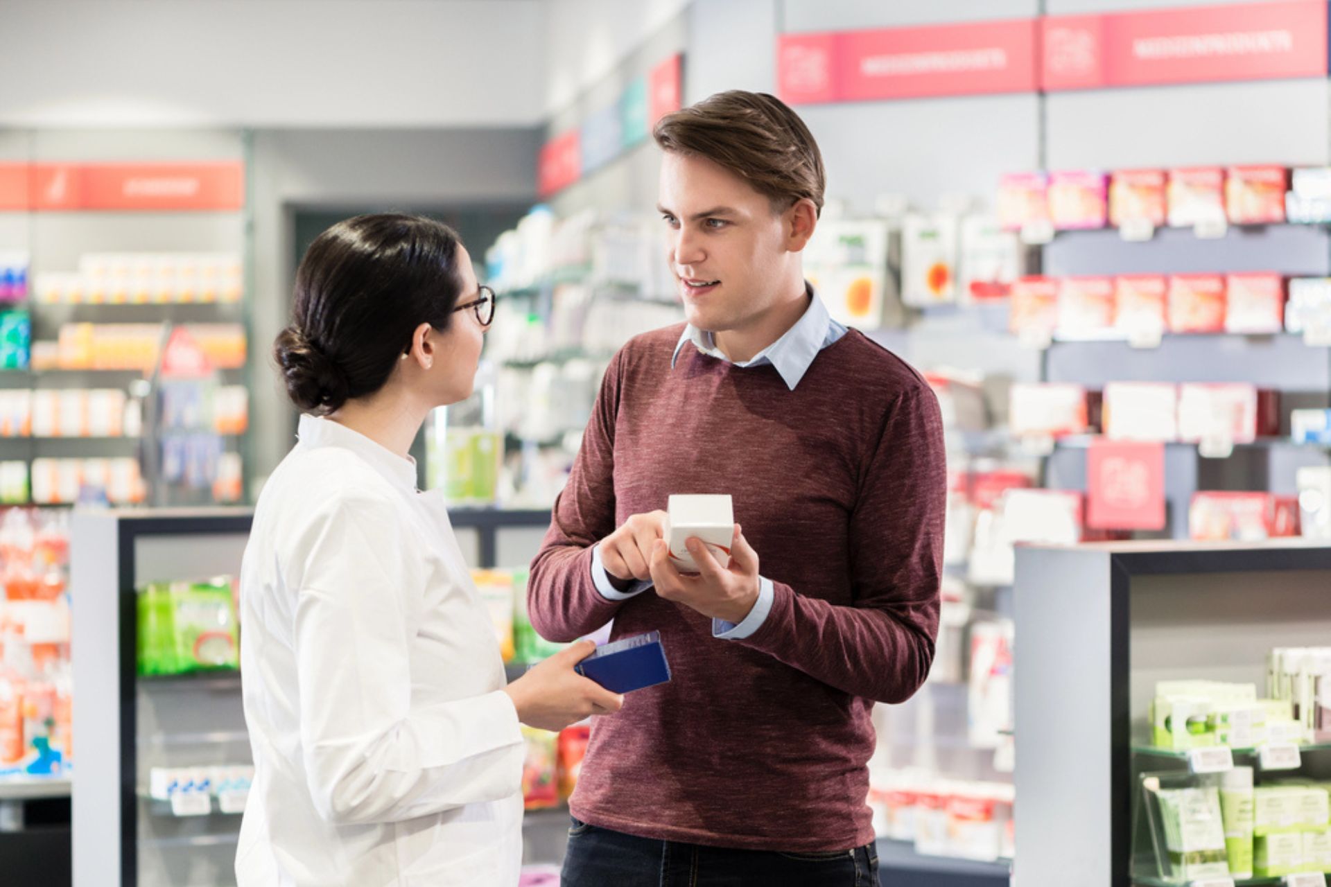 Un pharmacien discute avec un client dans une pharmacie lumineuse, illustrant l'importance de la gestion des réclamations pour améliorer la satisfaction et fidéliser les patients.