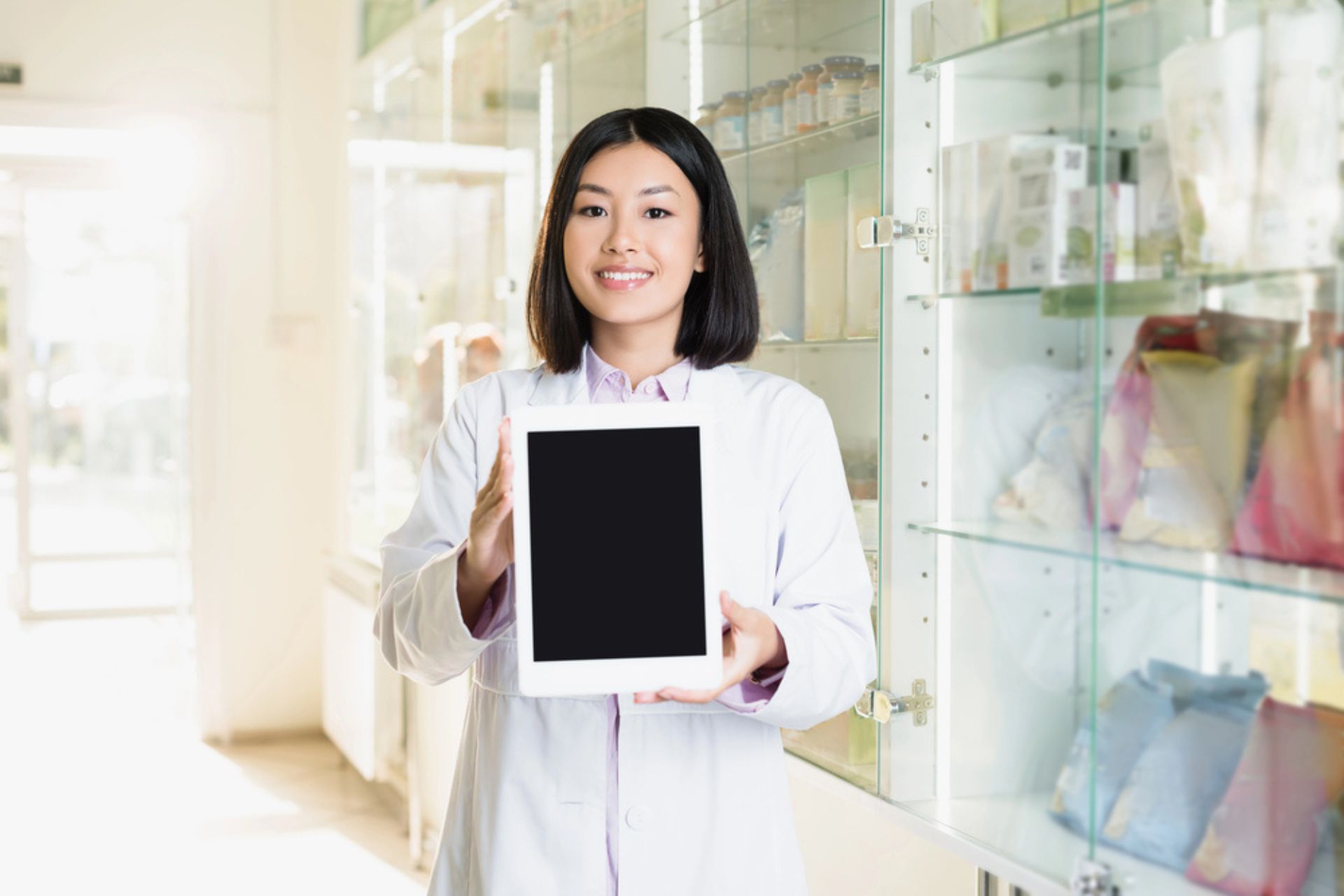 Pharmacienne souriante présentant une tablette numérique dans une officine moderne – Illustration de la transformation digitale en pharmacie avec une plateforme qualité.