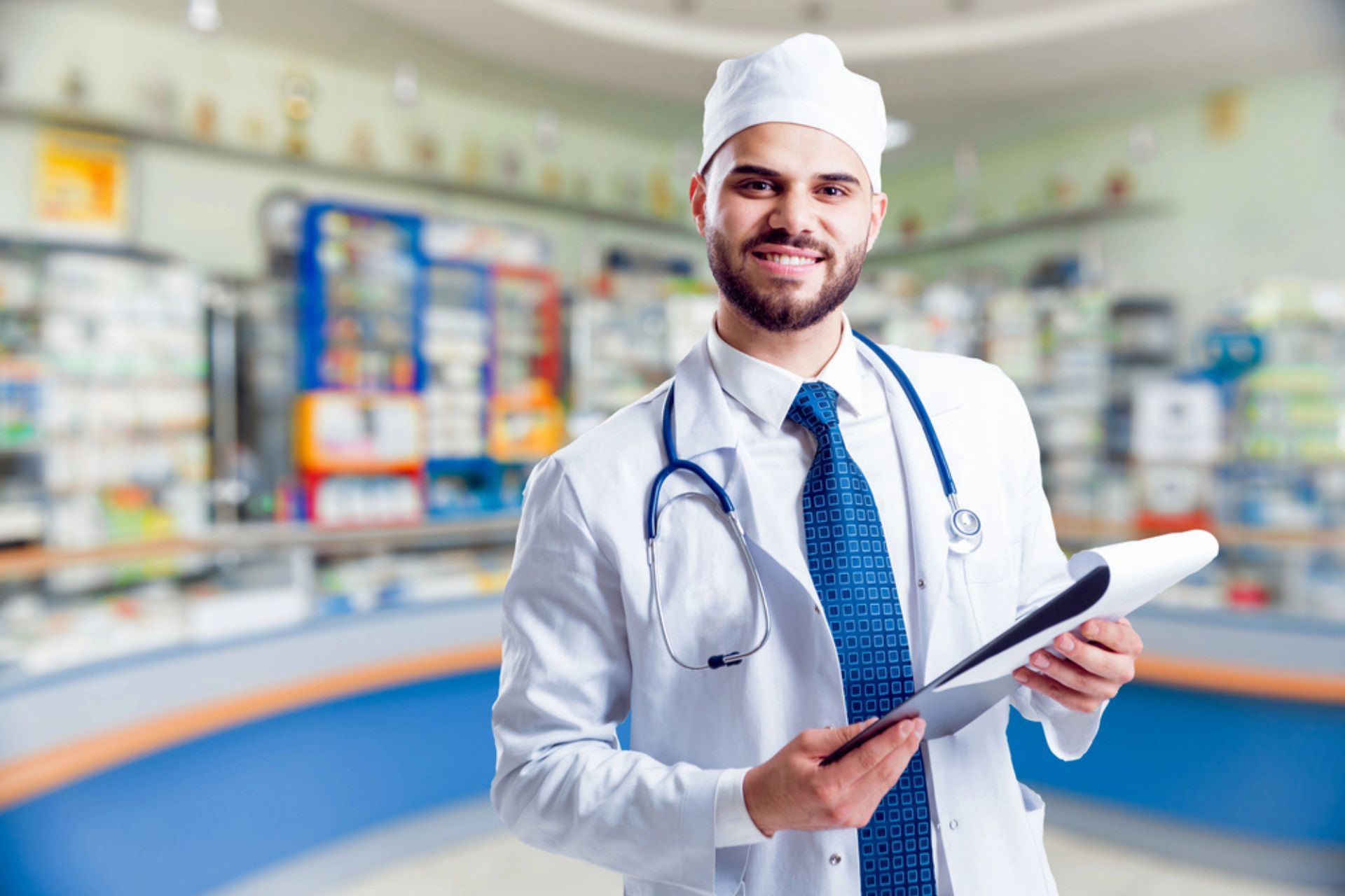 Pharmacien souriant en blouse blanche avec un stéthoscope, tenant un dossier dans une officine moderne, symbolisant l'implication de l'équipe dans la qualité des services pharmaceutiques.